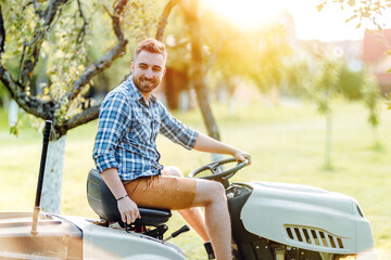 Wall Mural - portrait of handsome smiling gardener, man trimming grass in garden using tractor