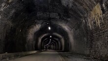 Distant Rear View Of Unidentifiable Curvy Woman Riding Bicycle Inside Of Dark Cressbrook Tunnel, Part Of Famous Monsal Trail In Peak District National Park, England, UK.