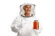 Mature male bee keeper in a uniform holding a jar of honey and pointing