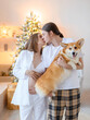 © IVASHstudio - Side view of love married couple expecting baby, beautiful pregnant woman lying on bed and touching belly and husband touching her head above while funny corgi sitting on background