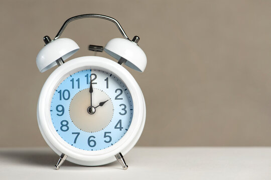 Two hours on the alarm. A white alarm clock is on a white table. The clock hand points to 2 o'clock. Translate of time. Set an alarm for 2:00 or 14:00. copy space
