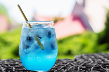 Wall Mural - Glass of tasty blue cocktail and yellow lemons on blured background..Alcohol juicy fruit blue cocktail with curacao liquor, ice cubes and blueberry in frozen glass