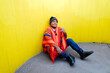 Young man with peruvian colorful poncho sitting in front of yellow wall