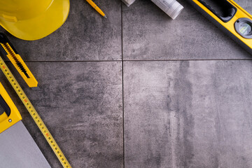 Contractor theme. Tool kit of the contractor: yellow hardhat, libella, hand saw. Plans and notebook on the gray tiles.