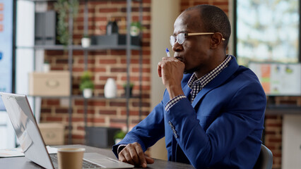 Wall Mural - Male consultant brainstorming ideas to create finacial project with business information, feeling pensive. Thoughtful worker thinking about strategy, pondering startup solution. Tripod shot.