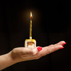 Roll with a festive candle on a female palm on a black background.