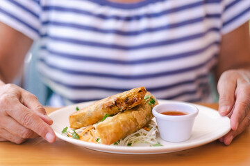 Wall Mural - Close-up on woman's hands ready to eat chinese spring rolls.  Blurred caucasian lady sitting at restaurant table enjoying oriental food