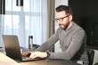 © Евгений Шемякин - Portrait of serious concentrated focused middle aged bearded man freelancer in glasses is working on his laptop computer, typing on keyboard at home at luxury apartment. Freelance distant job concept.