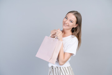 Wall Mural - View lovely slim cheerful girl holding package bag, dancing with pleasure, isolated on gray pastel color background in light clothes. Beautiful young woman rejoices in shopping, mock up and copy space