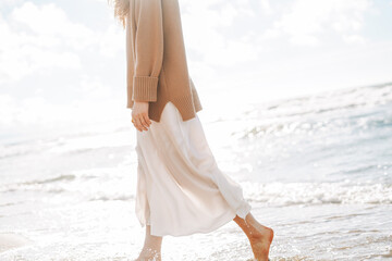 crop photo of young beautiful woman in beige sweater enjoying life on sea beach on sunset