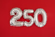 From above of silver shiny balloons demonstrating number 250 two hundred and fifty on red background with scattered glitter