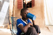 African village boy sitting in a sunny courtyard drinking from a big blue plastic mug; scarcity of water supply to private households in West African landlocked countries
