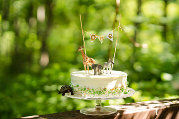 Minimalism birthday cake in scandinavian style for baby for first year birthday. On natural background, with animal toys decor. Photo zone for toddler. Eco birthday party.