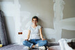© contrastwerkstatt - Young woman sitting in the floor, renovating her apartment and looking at the camera