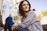 Fototapeta Panele - happy smiling young woman sitting in city looking to the side