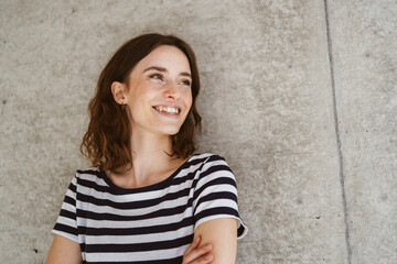 Wall Mural - Young happy woman stands in front of modern brown wall and looks to the side laughing