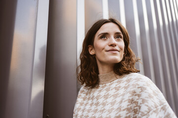 Wall Mural - Young smiling woman stands in front of modern steel wall and looks up