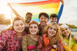 Young diverse people having fun holding LGBT rainbow flag outdoor - Focus on asian guy face