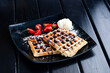 Plate of belgian waffles with chocolate sauce and ice cream on dark background