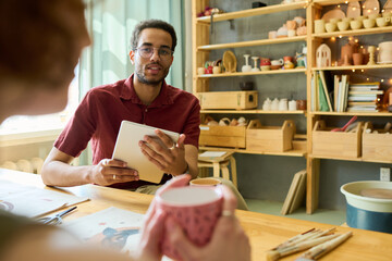 Aufkleber - Young black man with tablet looking at female colleague during discussion of ideas for new creative project in workshop