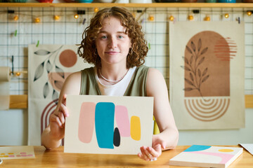 Aufkleber - Young smiling female holding abstract painting created by herself while showing it to you and looking at camera in workshop or studio