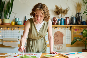 Aufkleber - Young creative female bending over table while painting abstract picture on paper with paintbrush and green watercolor in workshop