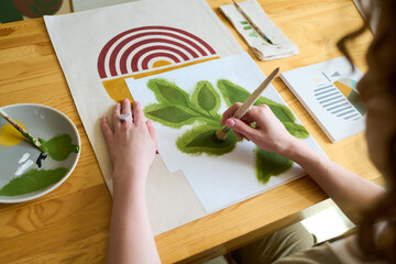 Aufkleber - Hands of young female student of art school painting green leaves with paintbrush and gouache on paper while sitting by table