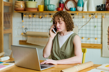 Aufkleber - Young confident female owner of craft shop talking on mobile phone and looking through online orders of clients in front of laptop