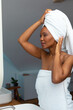African american young woman adjusting her white head towel in bathroom at home, copy space