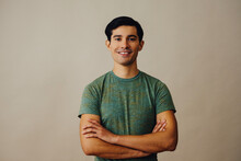 Portrait Hispanic Latino Man With Arms Crossed And Black Hair Smiling Handsome Young Adult Green T-shirt Over Gray Background Looking At Camera Studio Shot