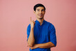 Portrait hispanic latino man with arms crossed pointing up at copy space black hair smiling handsome young adult blue shirt over pink background looking at camera studio shot
