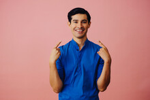 Portrait Hispanic Latino Man With Arms Crossed Pointing At Himself Black Hair Smiling Handsome Young Adult Blue Shirt Over Pink Background Looking At Camera Studio Shot