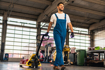 Caucasian professional male mechanic pulls, trolley with repair parts. Service, maintenance, people concept. Side view. Selective focus. Web Banner