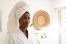 Young African American Woman Wearing Head Towel And Bathrobe Looking Away In Bathroom At Home