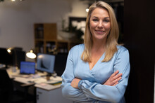 Portrait Of Smiling Confident Female Professional With Arms Crossed Standing In Office At Night
