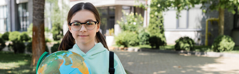 Sticker - Preteen schoolchild in eyeglasses holding globe and looking at camera outdoors, banner.