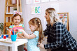 © Татьяна Волкова - Happy little girls and educator studying, playing and folding cubes on desk sitting on floor in playroom side view. Interesting lesson for kindergartners developing logic and intelligence