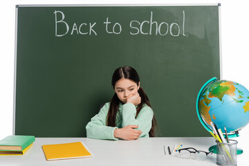 Wall Mural - Sad pupil sitting near books on table and chalkboard with back to school lettering isolated on white.