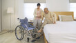 Asian woman nurse, daughter help father to get up from bed to wheelchair, supporting old senior elderly patient in bedroom in home or house in healthcare. People lifestyle. Family disability therapy.