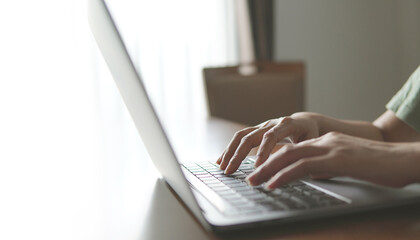 Hand taping keyboard of laptop on wooden table.