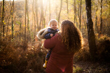 A Woman With Curley Red Hair Holding A Smiling Baby In A Forest