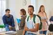 © Studio Romantic - Portrait of happy dark skinned male university student with copybook and backpack. Young man with sincere wide smile smiles at camera while standing in classroom against background of his classmates.
