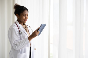 African doctor holding tablet for work and looking to something at beside curtain