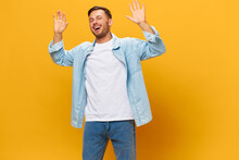 Friendly Happy Tanned Handsome Man In Blue Basic T-shirt Raise Hands Up Waving At Camera Posing Isolated On Orange Yellow Studio Background. Copy Space Banner Mockup. People Emotions Lifestyle Concept