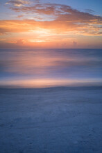 A Long Exposure Of A Calm Sea Reflecting A Sunset With A Sandy Beach Foreground