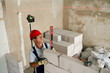 Bricklayer or mason lays bricks to construct wall of autoclaved aerated concrete blocks. Brickwork worker contractor doing precise masonry of foam concrete with spirit and laser levels.