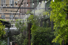Fogging Outdoor Cool Misting System Working Hot Summer Day For Terrace In Cafe. Facility That Lowers Temperature By Spraying Fine Mist. Air Conditioning And Water Spray System For Cooling And Fog.