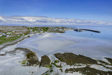 View on Inishmore harbor and pier and beach and town building. Warm sunny day. Cloudy sky. Popular travel and tourism area with amazing nature scene. Aran islands, county Galway, Ireland.