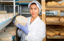 Portrait Of Skilled Asian Woman Working In Storehouse At Cheese Factory, Controlling Maturing Process Of Goat Cheese Wheels Placed On Shelves
