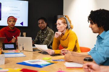 Serious female caucasian app developer with colleagues in board room at office